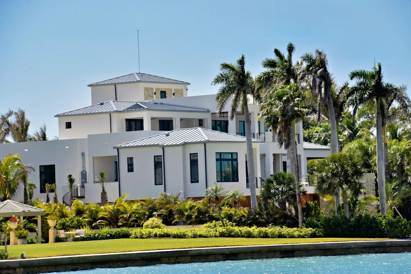 A white Florida home with a metal roof behind palm trees on the water